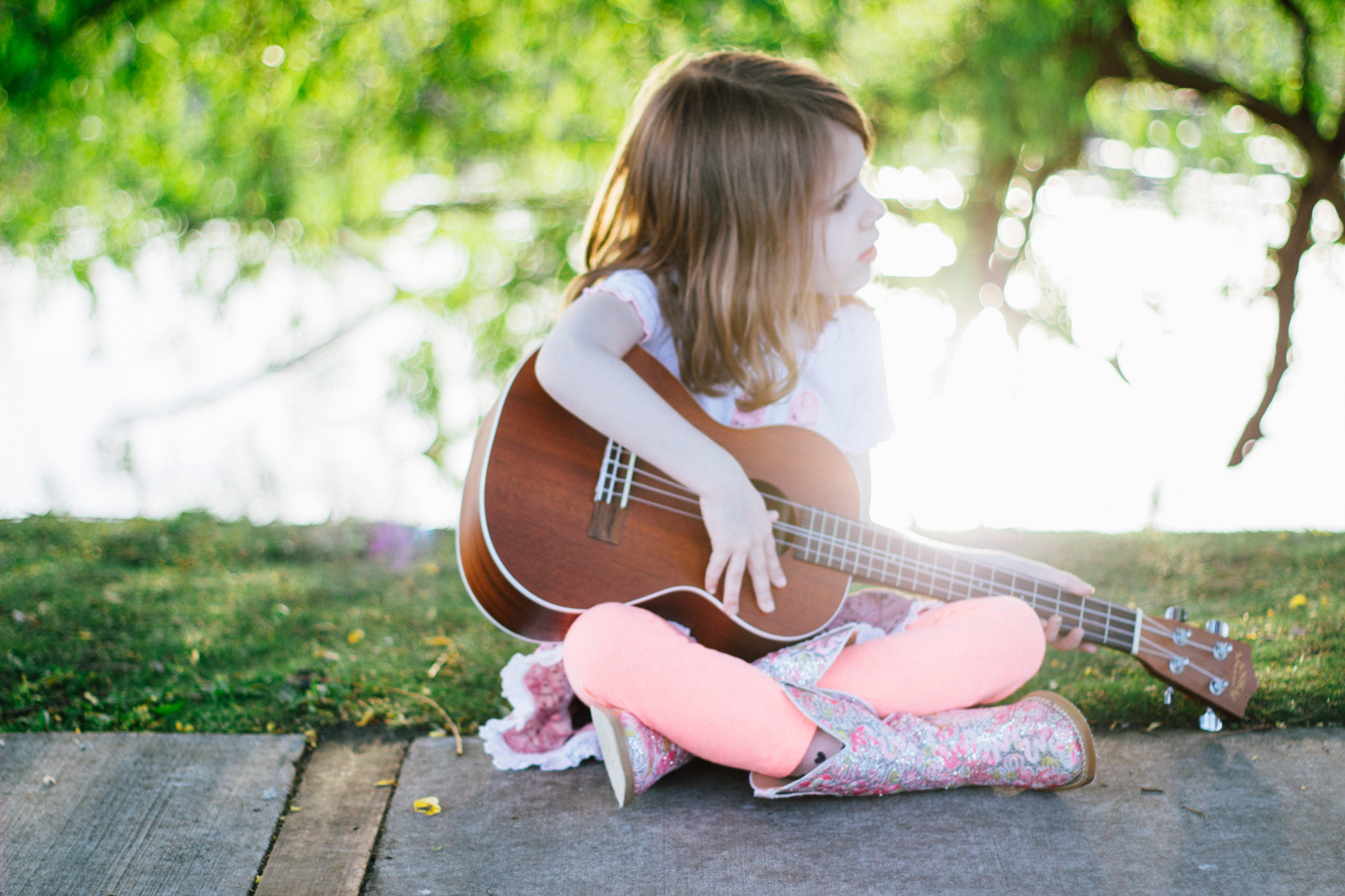 a-young-girl-playing-ukulele-in-a-park-under-a-tree-at-sunset_t20_AepE11