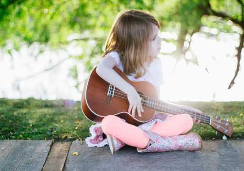 a-young-girl-playing-ukulele-in-a-park-under-a-tree-at-sunset_t20_AepE11